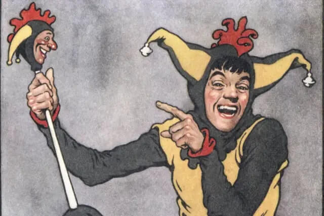 A lively performer dressed in a black and yellow jester costume with red accents, smiling broadly and pointing with one hand while holding a staff topped with a miniature jester head that mirrors his own appearance.