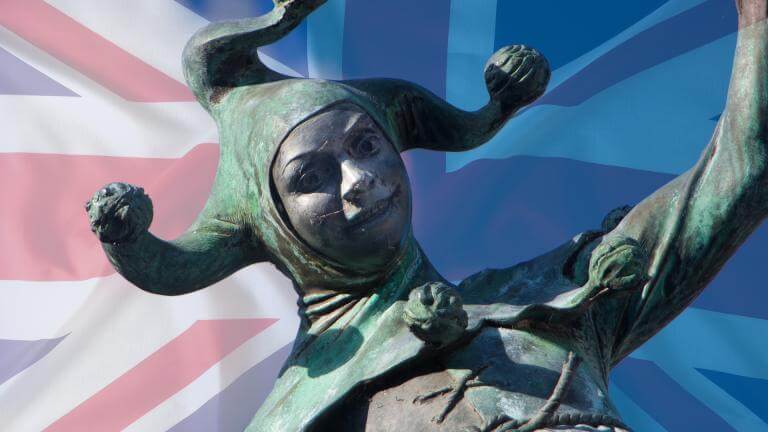 A bronze statue of a jester wearing a multi-pointed hat with ball tips, captured mid-gesture with one arm raised in playful expression. Behind the figure, a stylized Union Jack flag blends into a blue-toned variation, creating a layered backdrop of British symbolism.