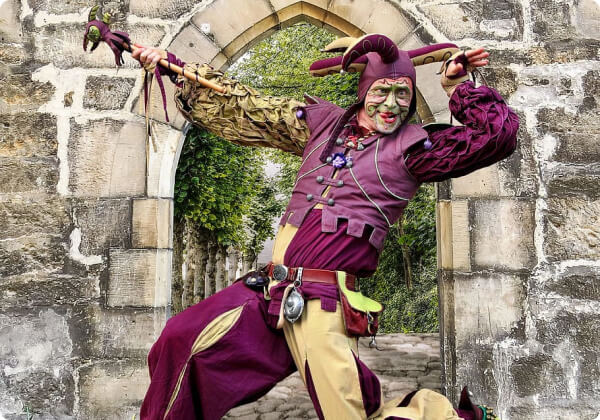 man in jester outfit in front of an old castle
