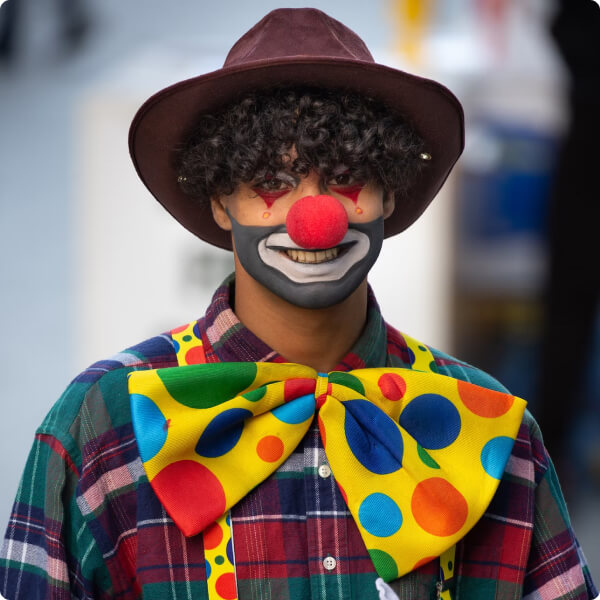 young clown with curly hair and a hipster hat in modern clown outfit