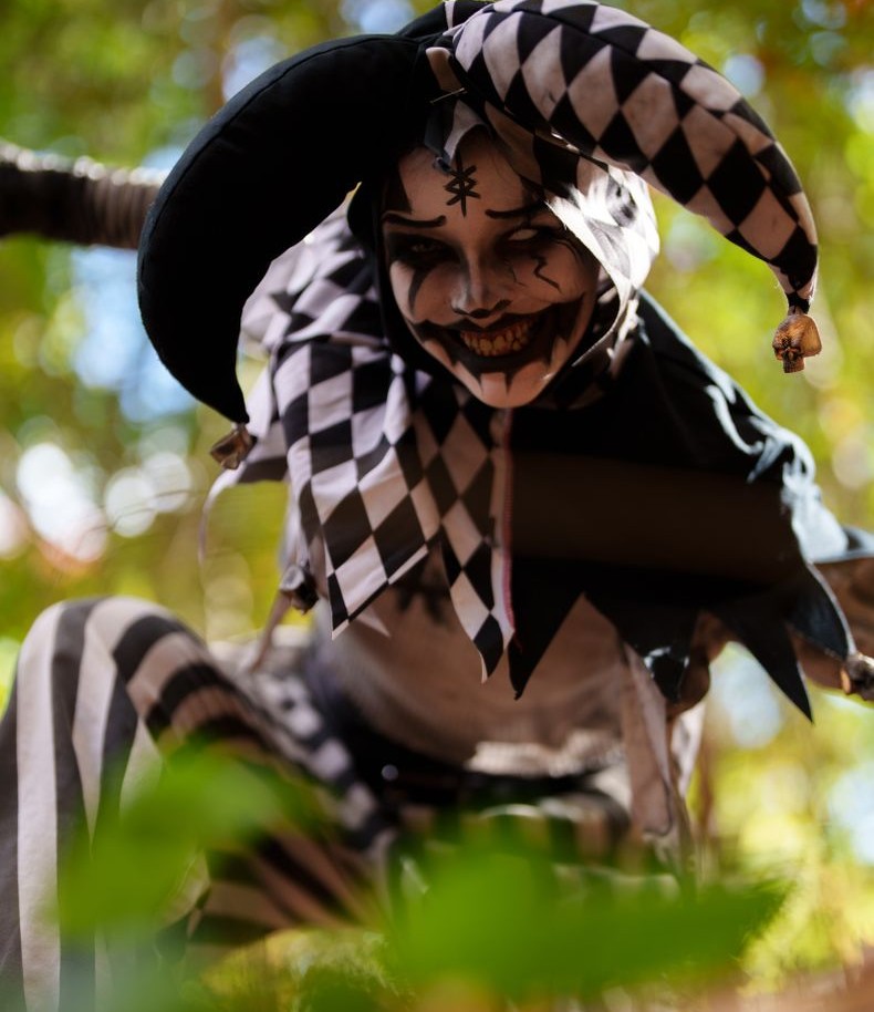 Person dressed as a jester with black and white costume in a forest.