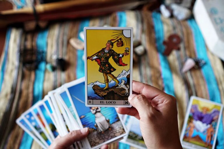 Hands holding tarot card 'El Loco' over striped cloth.